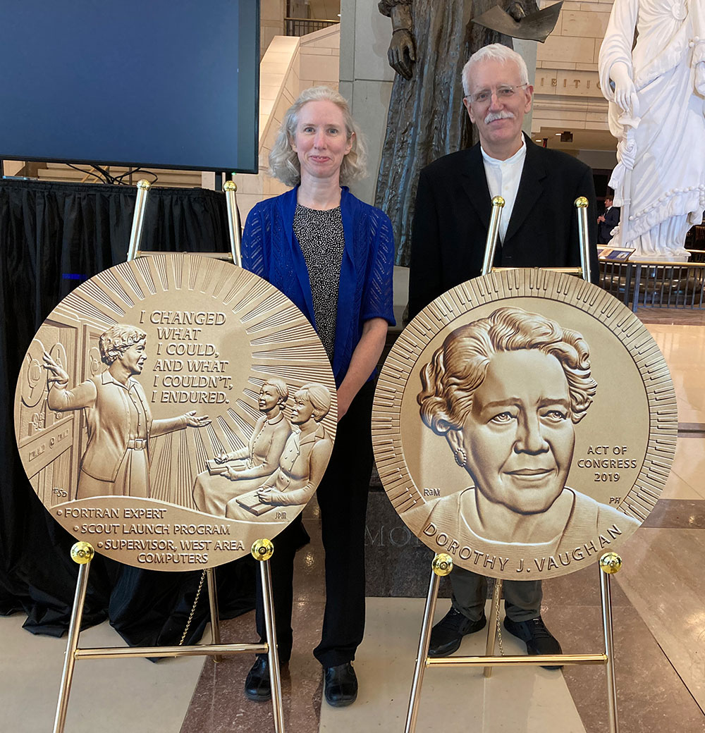 Photo showing Images of the Dorothy Vaughan Congressional Gold Medal, with its designers Emily S. Damstra and Richard A. Masters standing behind the reproductions